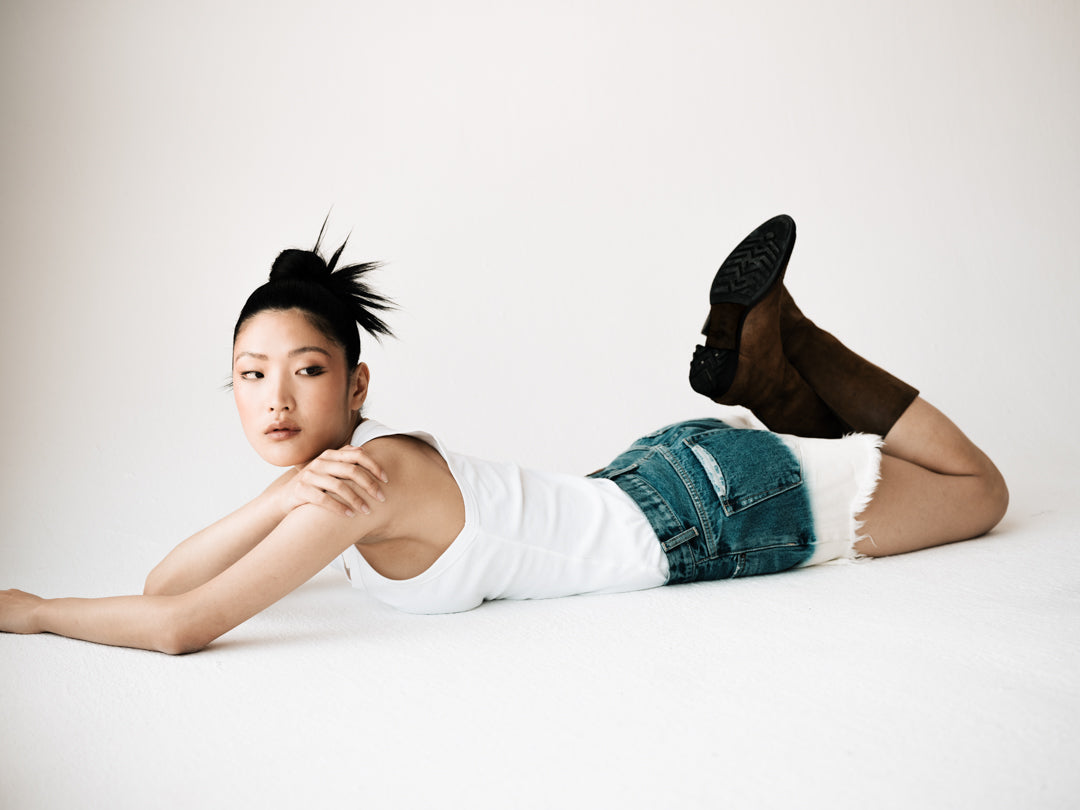 Fit model laying on her stomach, showcasing the B O R O デニム (BORO DENIM) 'Nagoya Let it Bleed' denim shorts. The shorts display a 2-tone bleached ombre effect on premium Japanese Selvedge Fabric, emphasizing their unique vintage design