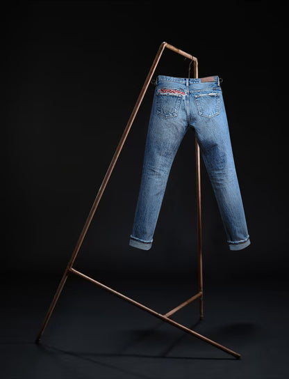 Sapporo jeans by B O R O デニム (BORO DENIM) in 'Gold in the Ceiling' wash hanging on a rack. The design accentuates the Japanese Selvedge fabric and vintage appeal, set against a black background showcasing the back side.