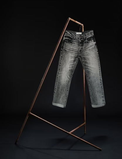 Front view of the B O R O デニム (BORO DENIM) 'Osaka Deep in the Heart' washed black jeans displayed on a rack against a black background. These jeans highlight the premium Japanese Selvedge Fabric and their distinctive vintage character
